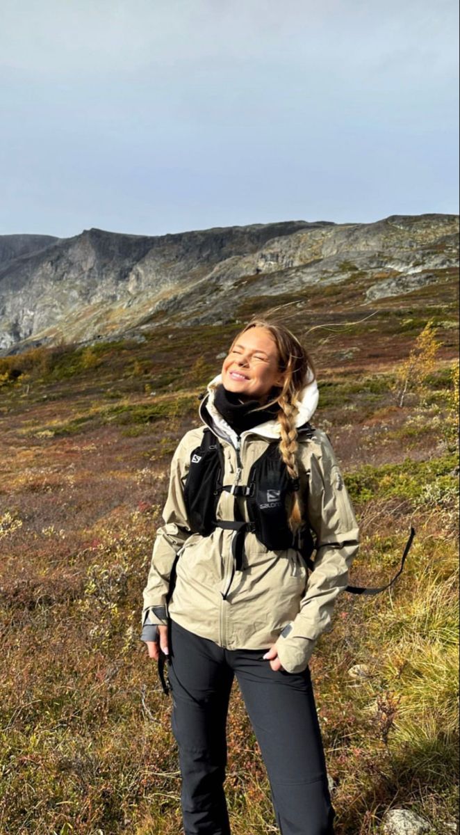 a woman standing on top of a grass covered field with mountains in the back ground