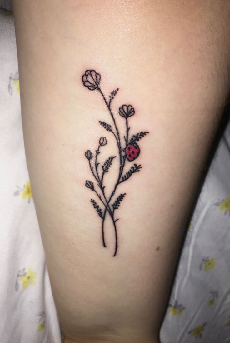 a ladybug tattoo on the leg of a woman's legs, with flowers and leaves