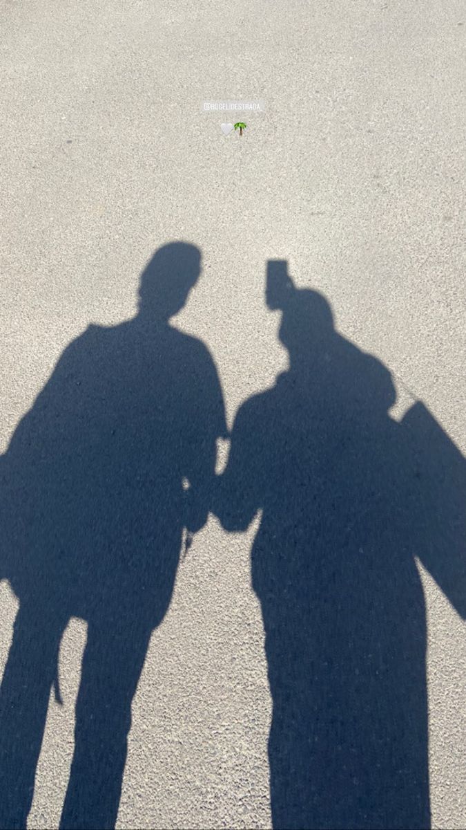 two people standing next to each other in the middle of an empty parking lot, casting a shadow