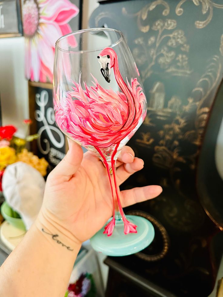 a hand holding a wine glass with pink flamingos painted on it