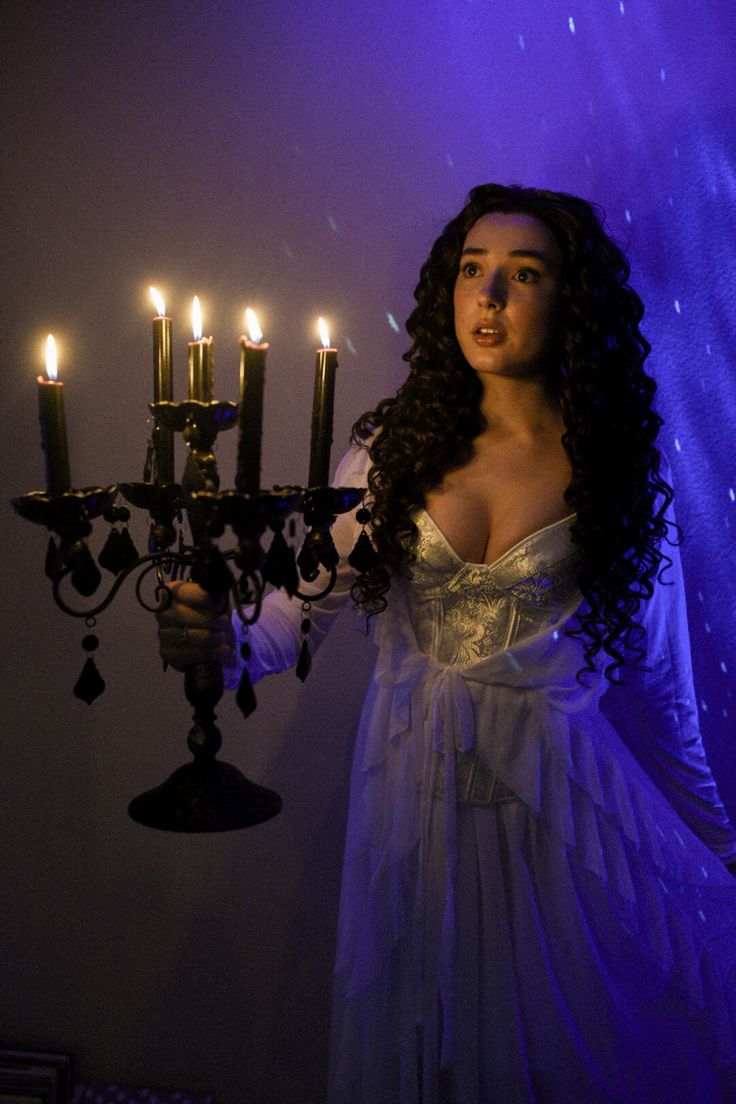 a woman in a white dress holding a candelabra with lit candles