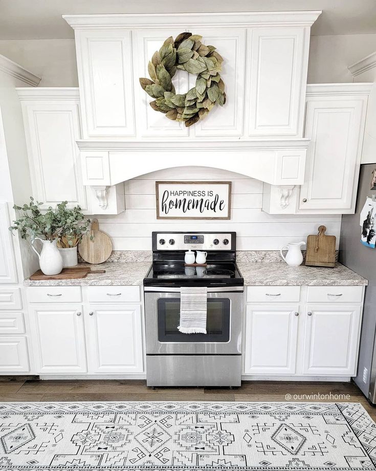 a kitchen with white cabinets and stainless steel stove top oven in front of a wreath on the wall