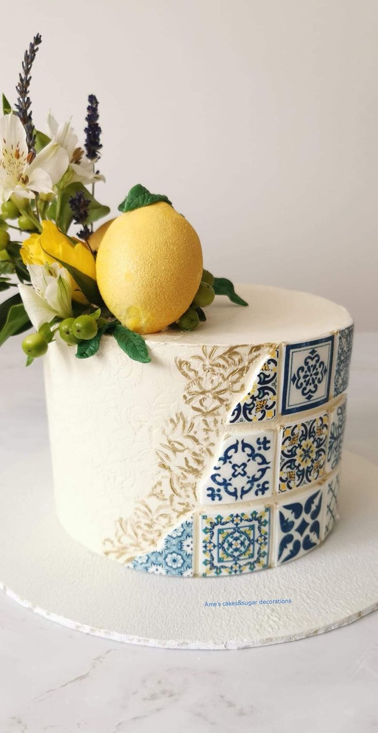 a white cake decorated with blue and yellow flowers, lemons and greenery on top