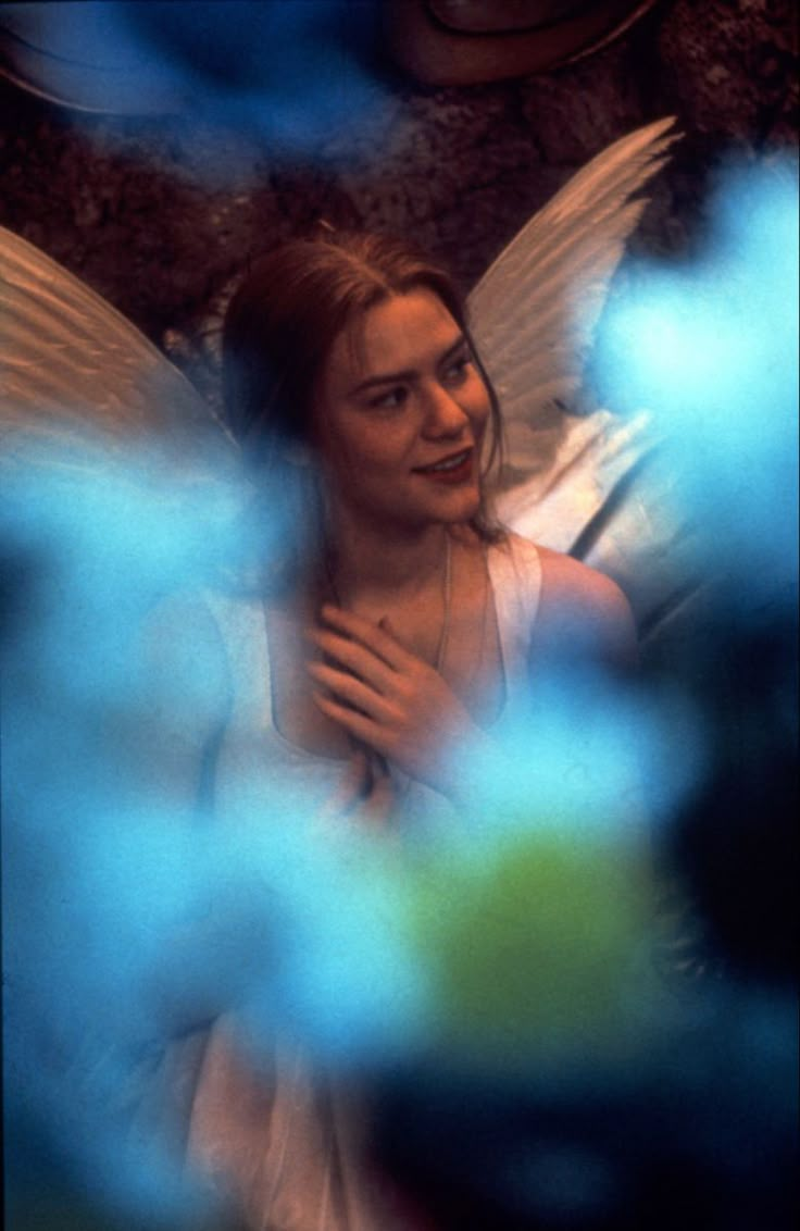 a woman dressed as an angel standing next to a blue flowery plant with white petals