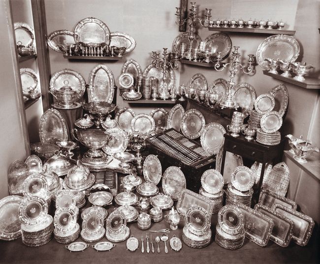 an assortment of glass and silverware on display in a room with shelves full of dishes