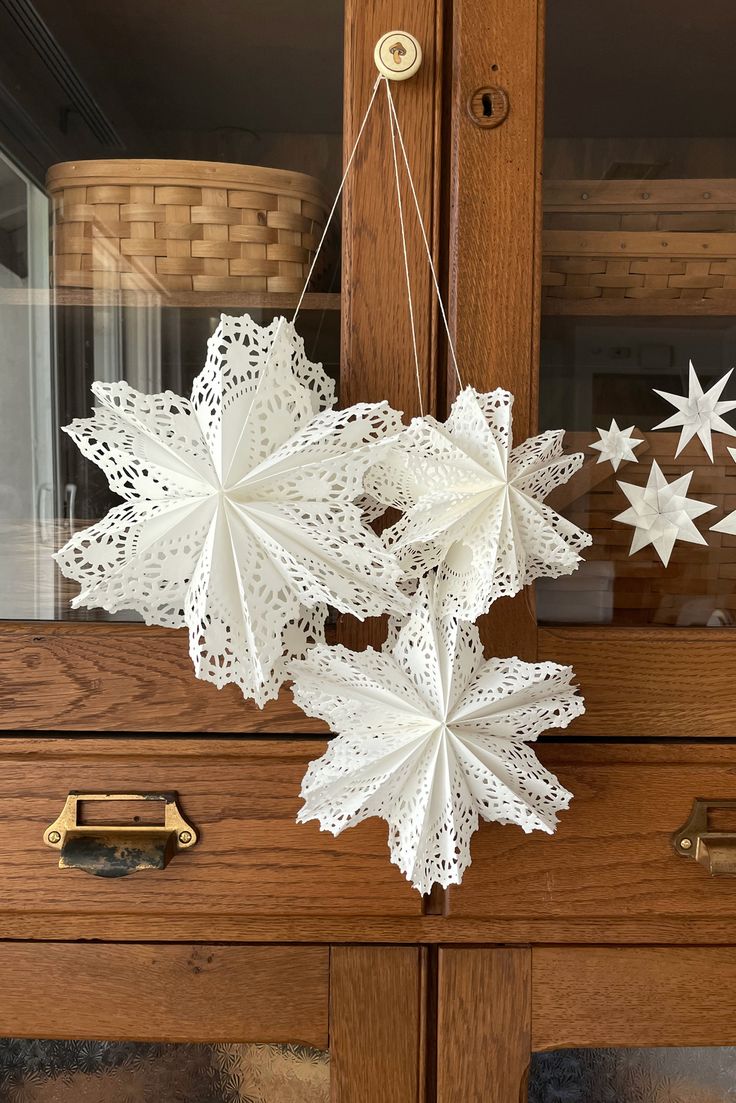 some white paper snowflakes hanging from a wooden cabinet