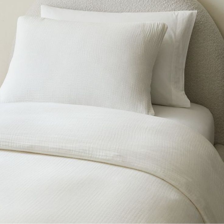 a bed with white sheets and pillows on top of it, next to a wall