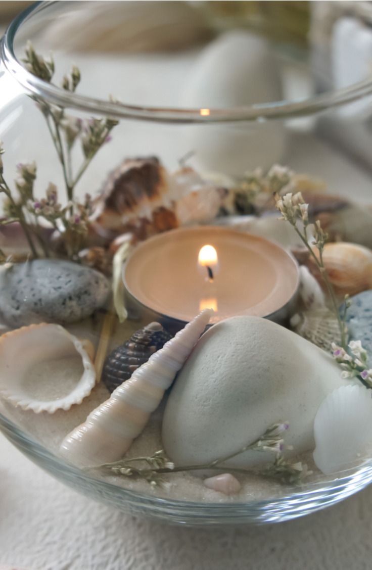 a glass bowl filled with sea shells and a lit candle