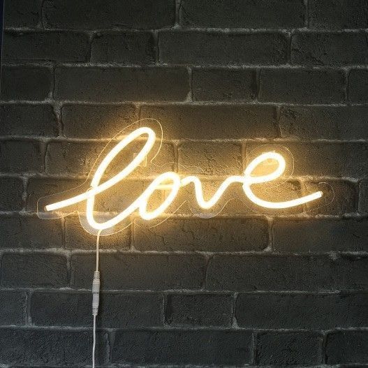 a neon sign that says love on a brick wall in front of a light bulb