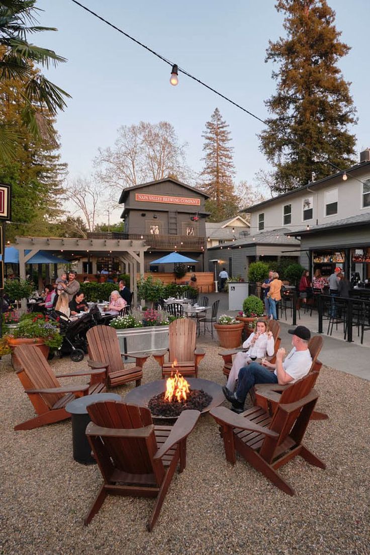 people sitting around an outdoor fire pit in the middle of a patio with tables and chairs