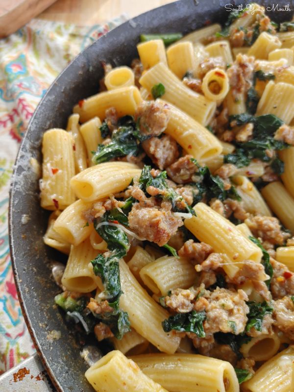 pasta with sausage and spinach in a skillet on a floral table cloth,