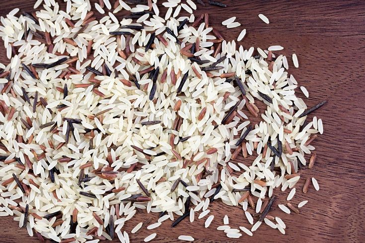 white rice on a wooden table with brown and black seeds in the middle, top view