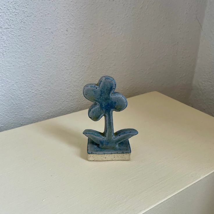 a small blue vase sitting on top of a white table next to a wall with a plant growing out of it