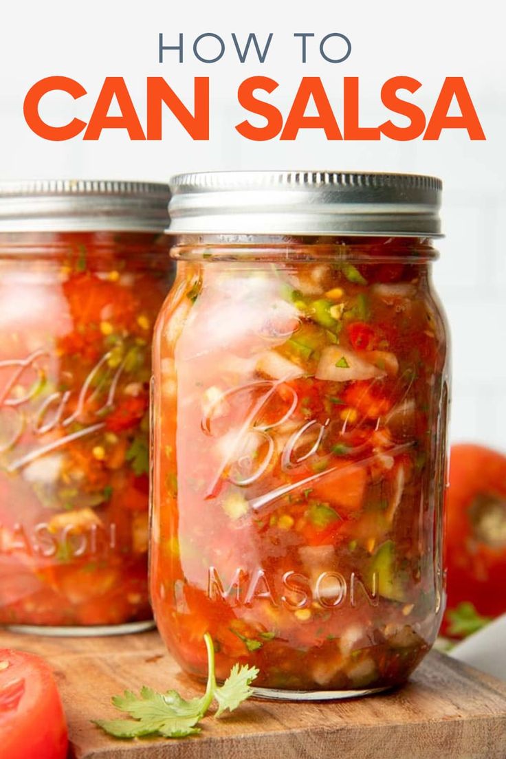 two mason jars filled with canned can salsa on top of a cutting board next to tomatoes