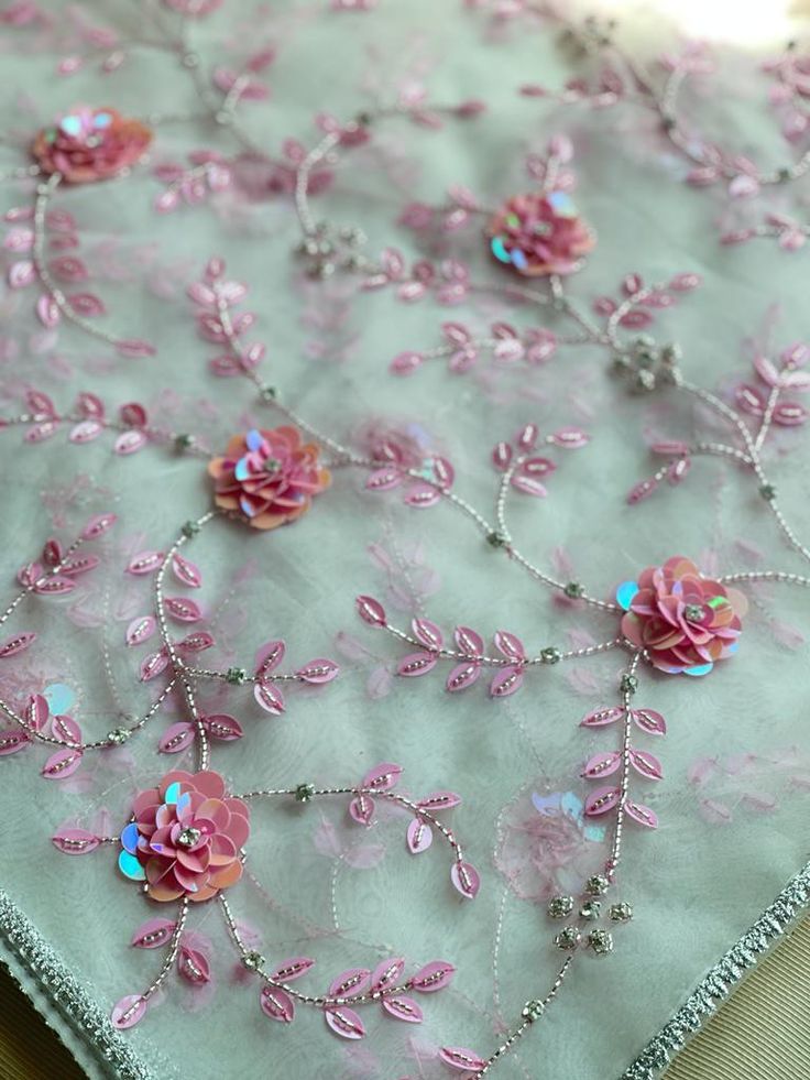 pink and blue flowers on light green fabric with silver beaded trim, closeup