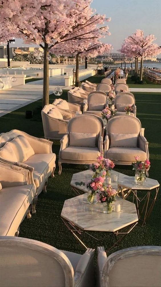 rows of couches and tables with flowers on them in front of the water's edge