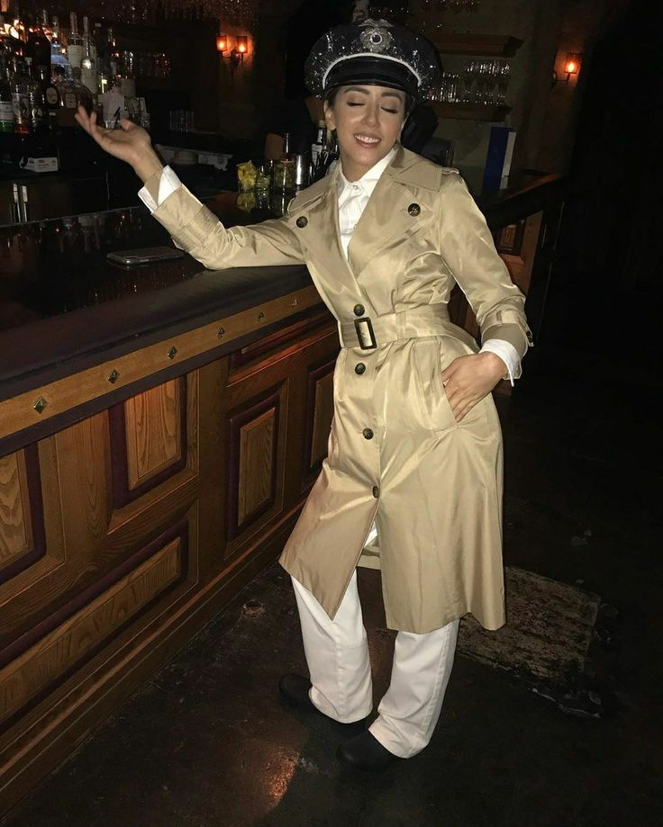 a woman in a trench coat and white pants standing next to a bar with her arms out