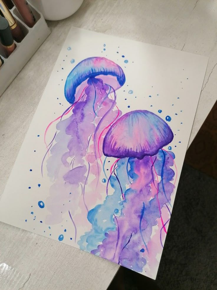 a watercolor painting of two jellyfish in purple and blue colors on white paper