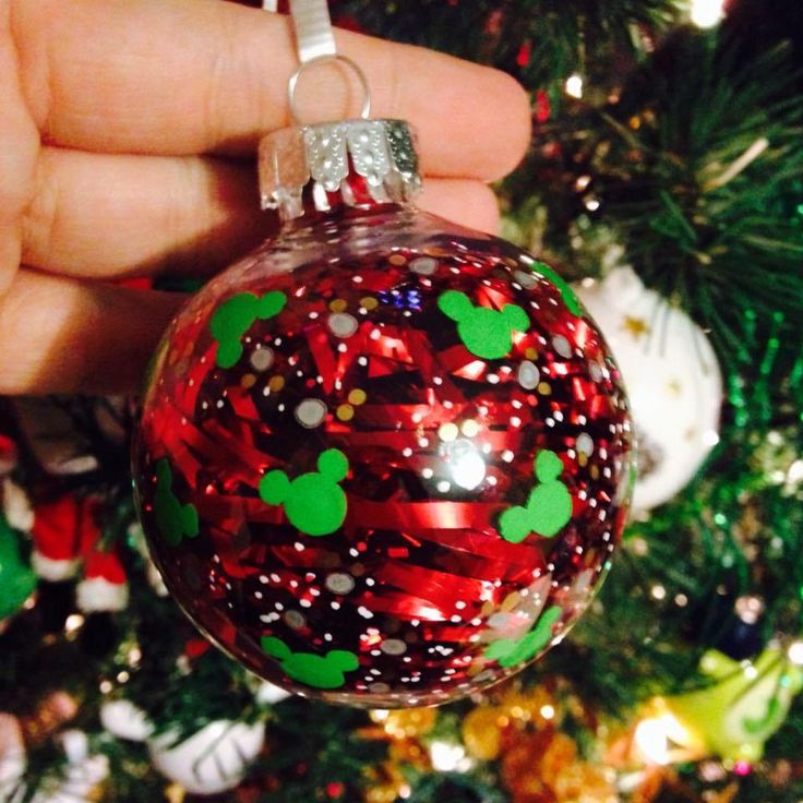 a hand holding a christmas ornament in front of a tree with ornaments on it