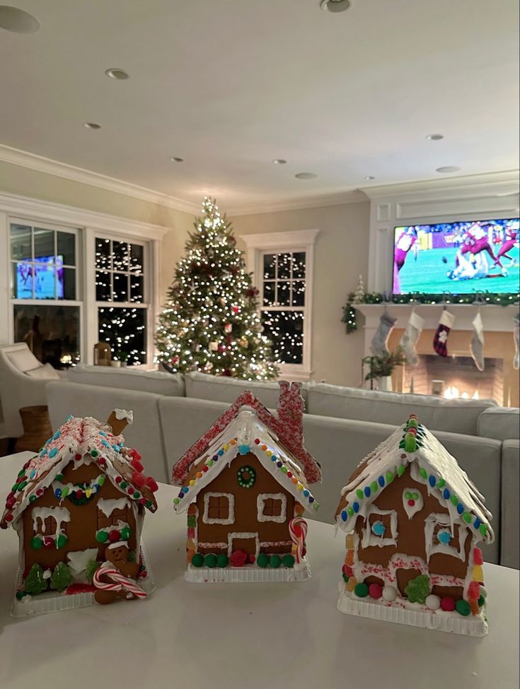 three gingerbread houses are sitting on a table in front of a christmas tree and television