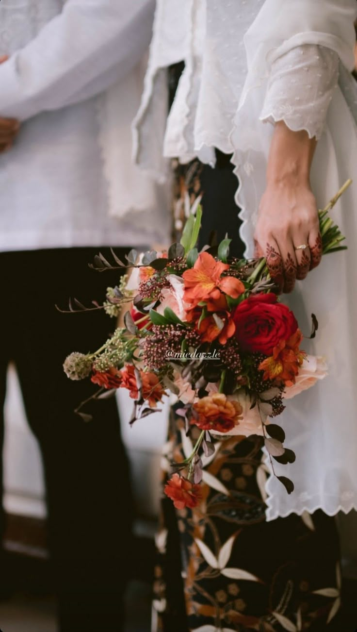 two people standing next to each other with flowers in their hands and one person holding the bouquet