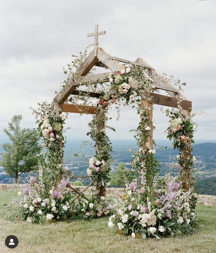 a wooden structure with flowers and greenery around it on the top of a hill