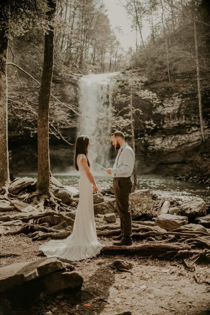 a bride and groom standing in front of a waterfall during their wedding ceremony at the falls