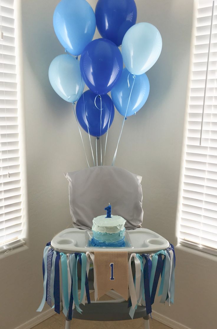 a table with a cake and balloons on it in front of a window that has shutters