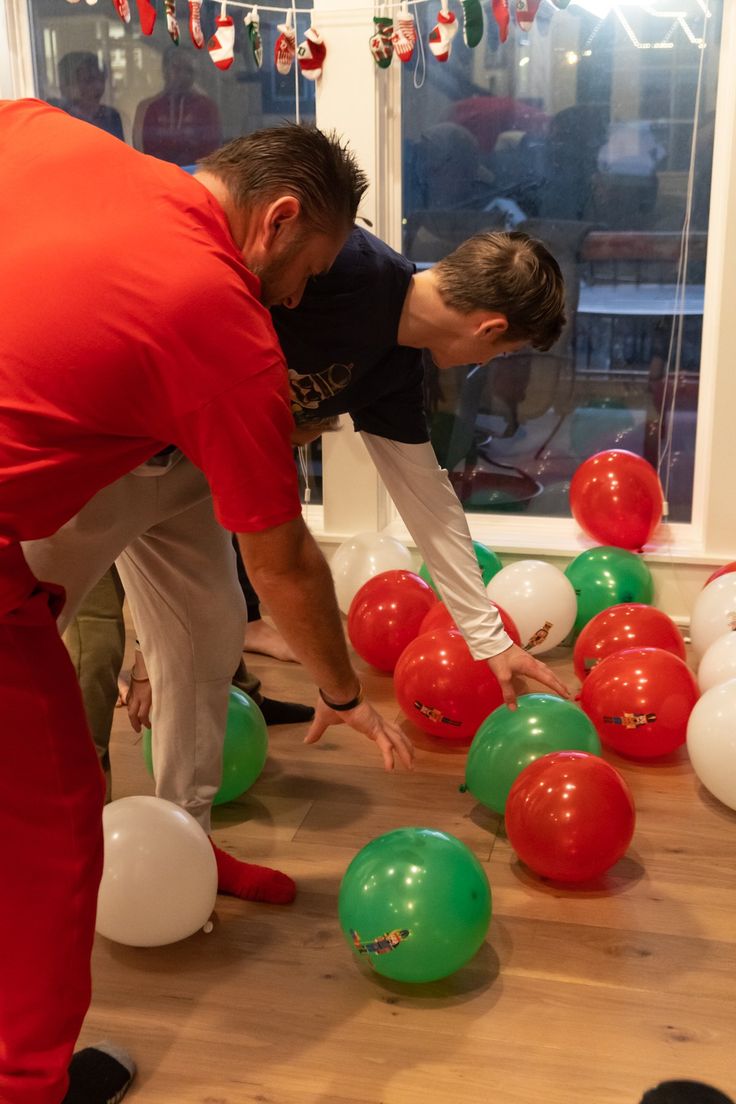 two men in red shirts and white pants playing with green and red balloons on the floor