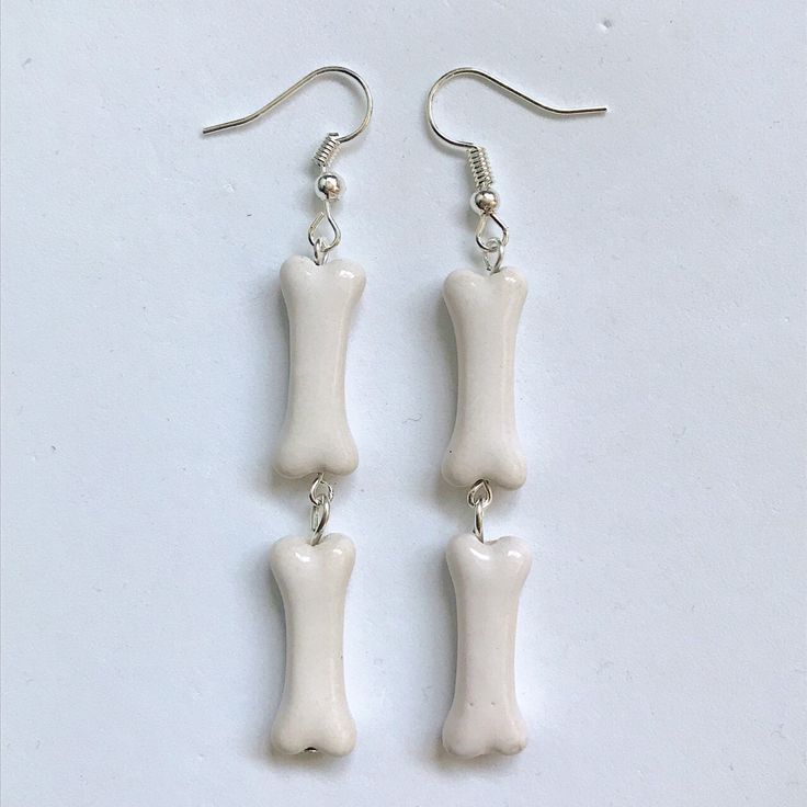 two bone shaped earrings are hanging from silver earwires