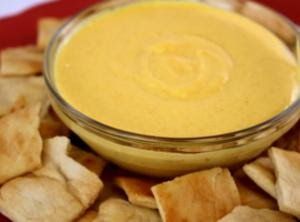 a red plate topped with crackers and a yellow dip in a bowl surrounded by chips