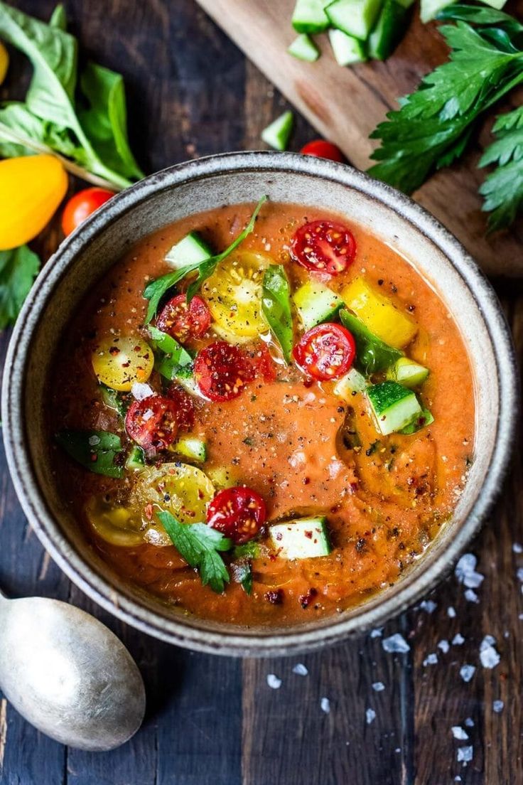 a bowl filled with tomato and cucumber soup on top of a wooden table