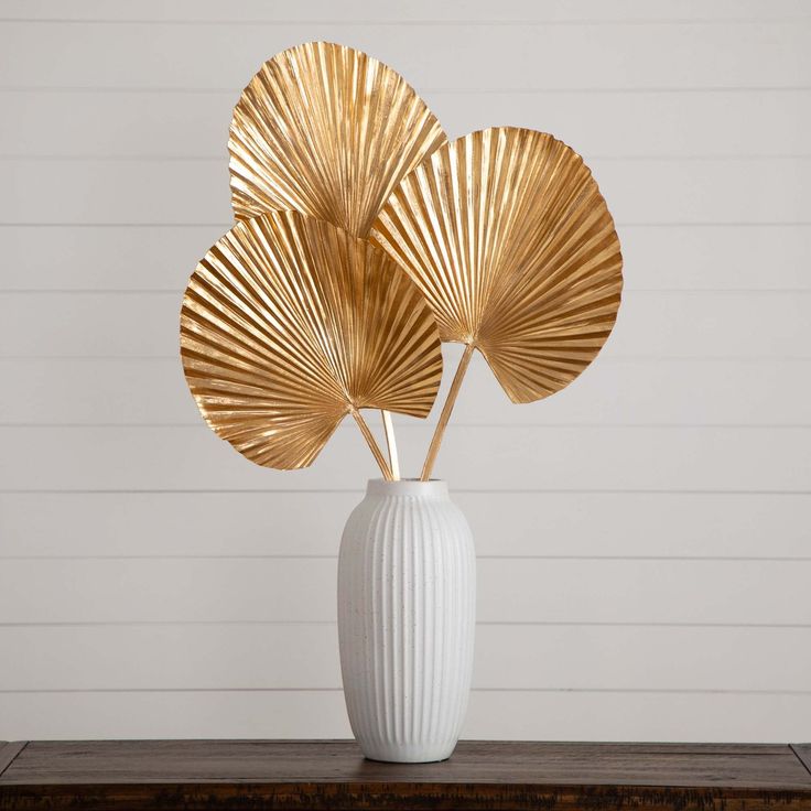 three golden leaves in a white vase on a table