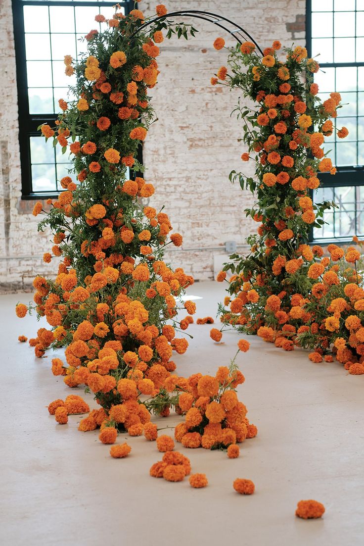 an arrangement of orange flowers on display in front of a brick wall and arched doorway