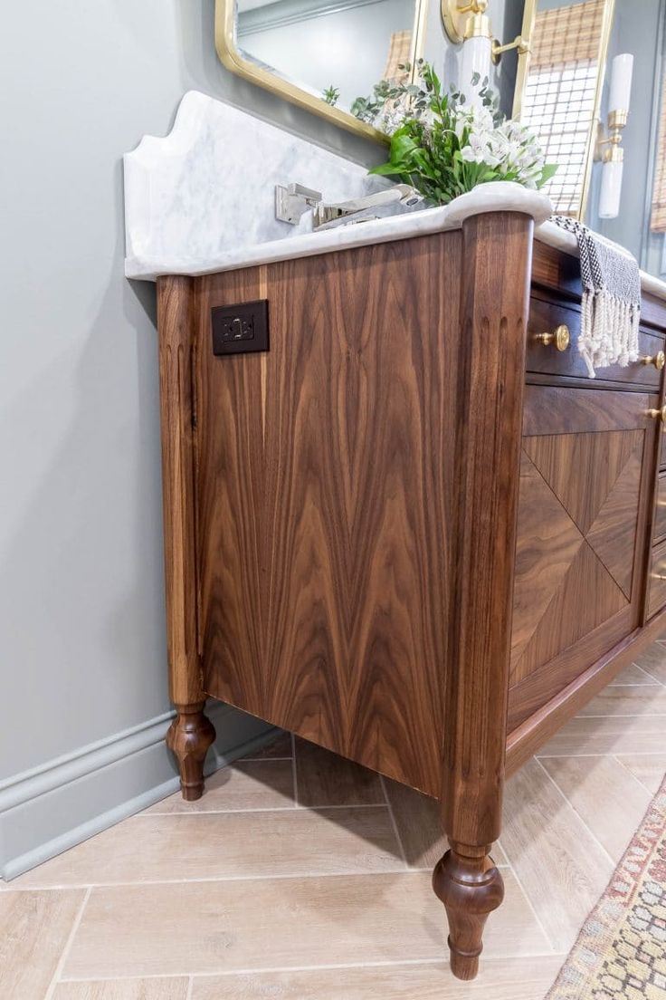 a bathroom vanity with a marble top and wooden legs, in front of a mirror