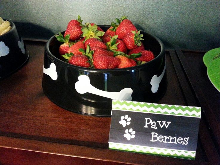 some strawberries are in a dog bowl on a table next to a sign that says paw berries