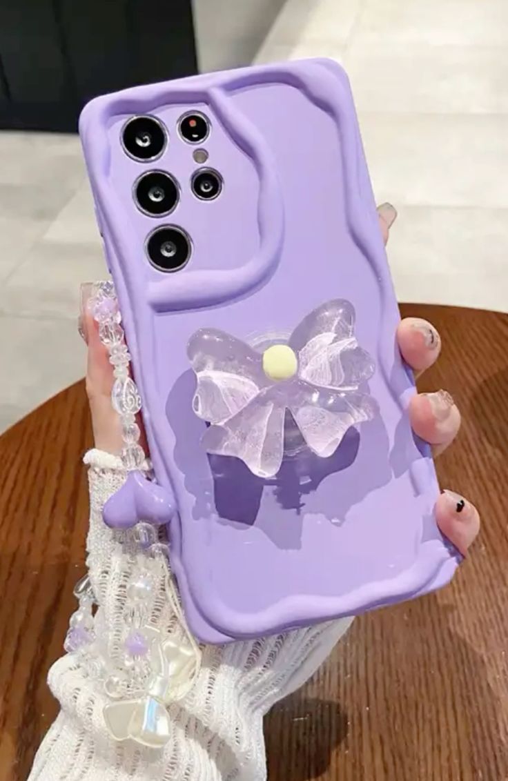 a person holding up a purple phone case with a bow on the front and side