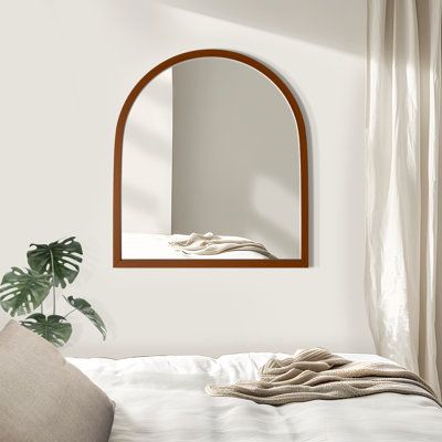 a bed with white sheets and a round mirror on the wall above it next to a plant