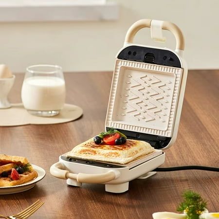 an electric waffle maker sitting on top of a wooden table next to plates of food