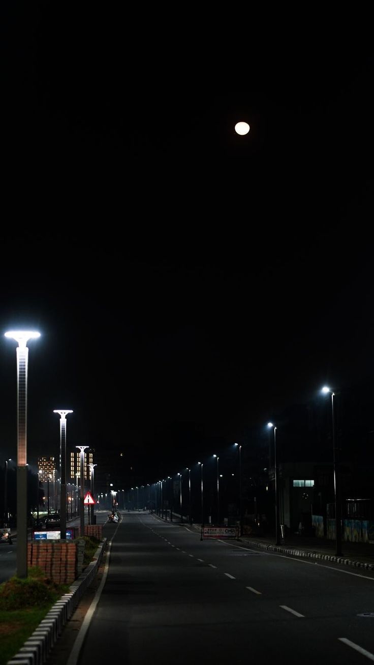 an empty street at night with lights on the sides and no cars parked along it