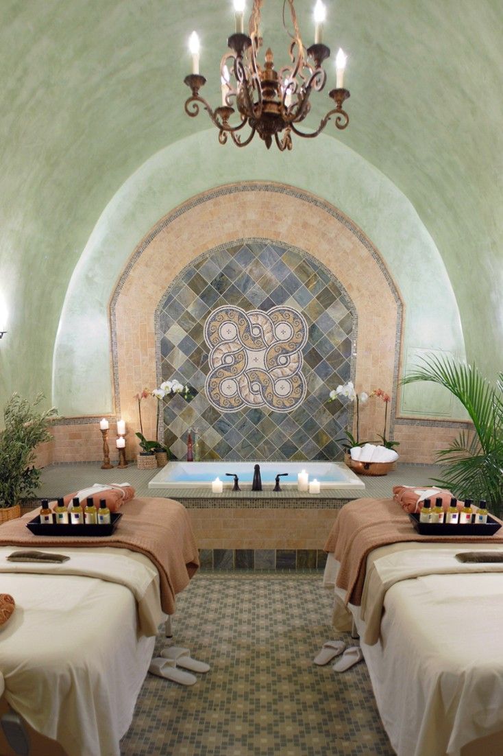 two massage tables with towels on them and candles in front of the bathtub that is surrounded by potted plants