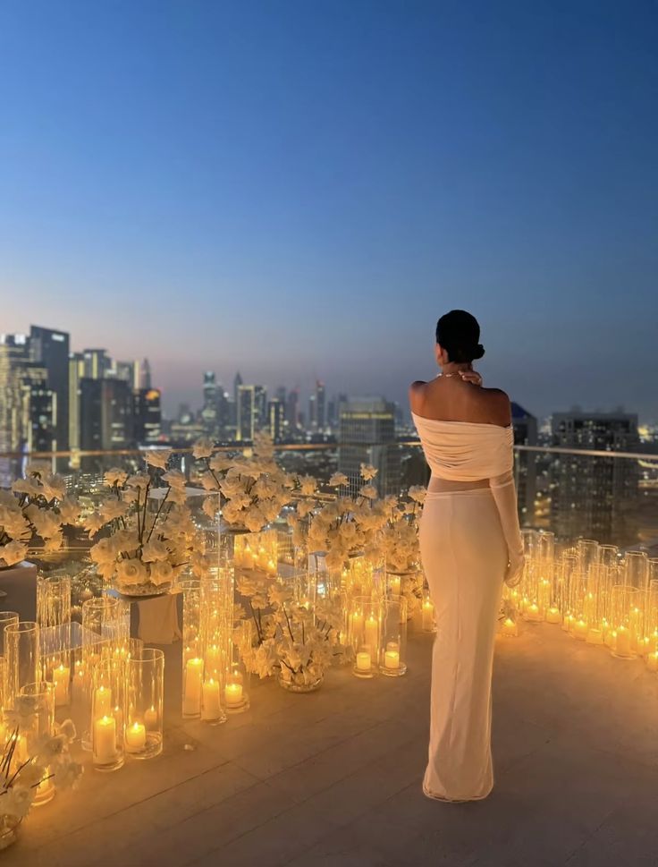 a woman standing on top of a roof next to tall glass vases filled with candles