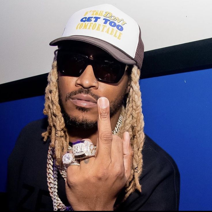 a man with dreadlocks wearing a hat and holding his finger up to the camera