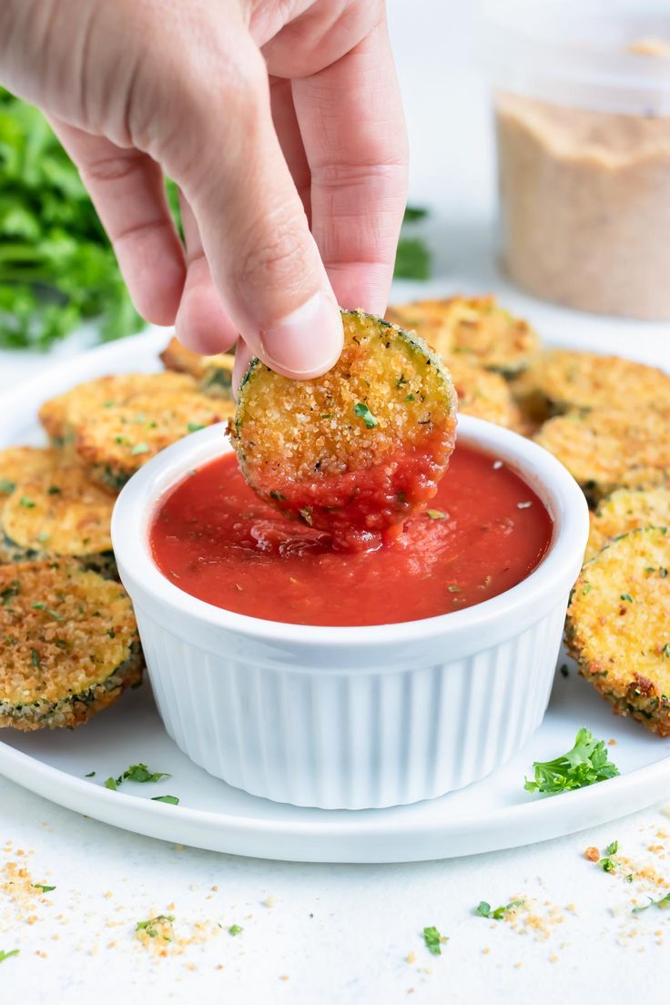 a person dipping some food into a small white bowl on a plate with other foods in the background