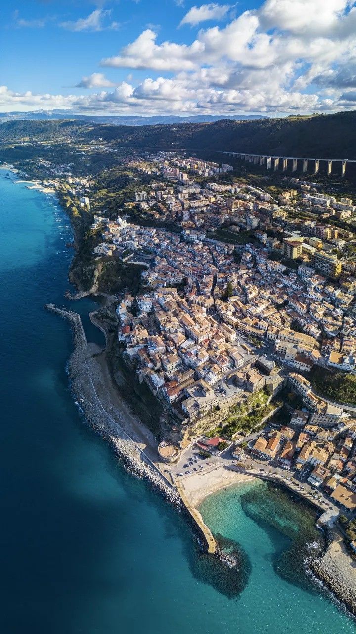 an aerial view of a city next to the ocean with blue skies and clouds in the background