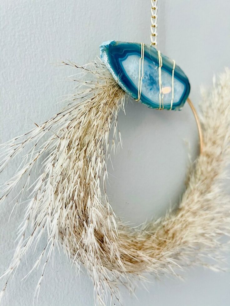 a piece of jewelry hanging from a chain on a white wall next to dried grass