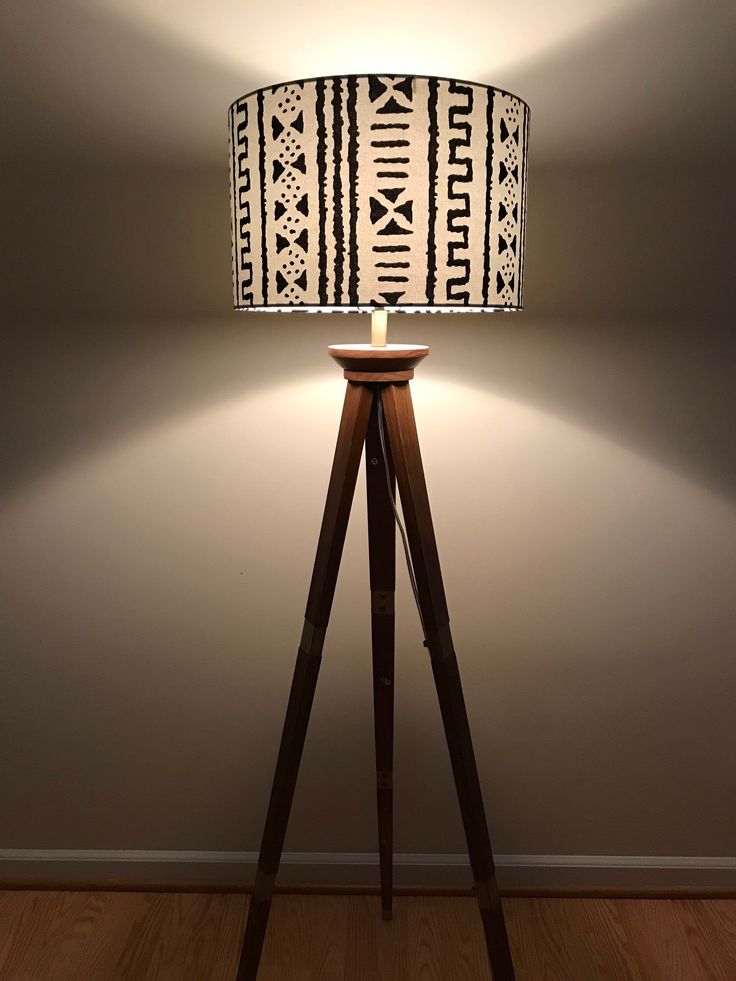 a lamp that is on top of a wooden tripod stand in front of a wall