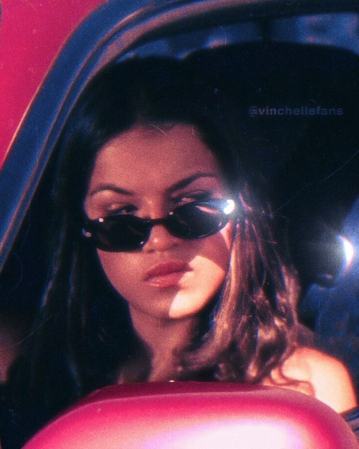 a woman wearing sunglasses sitting in the back seat of a red car with her head out the window