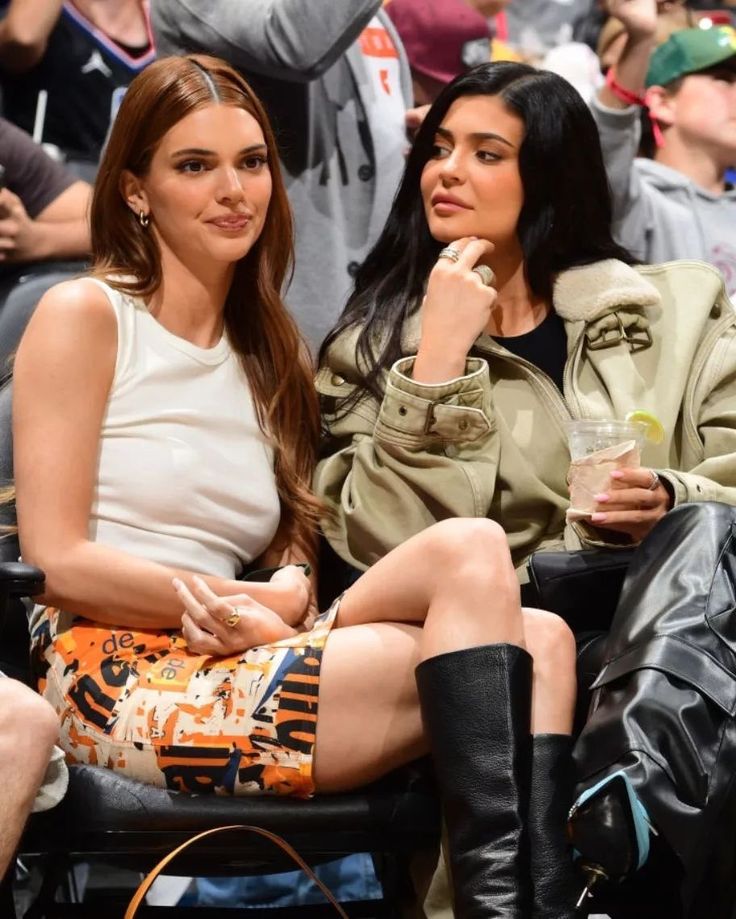 two women sitting next to each other in front of a crowd at a basketball game