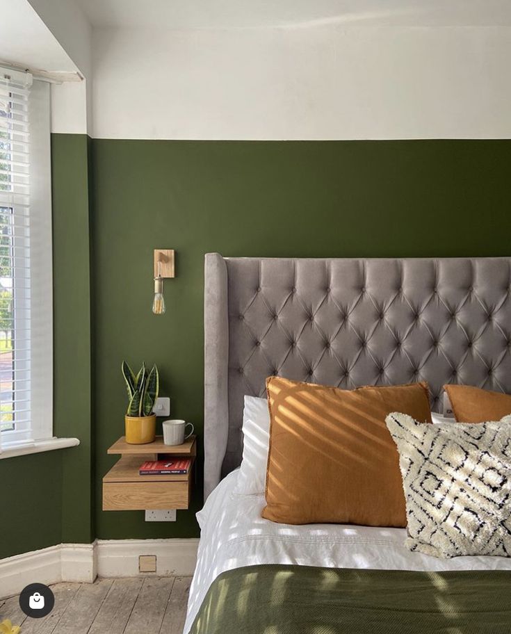 a bedroom with green walls, white bedding and orange pillows on the headboard